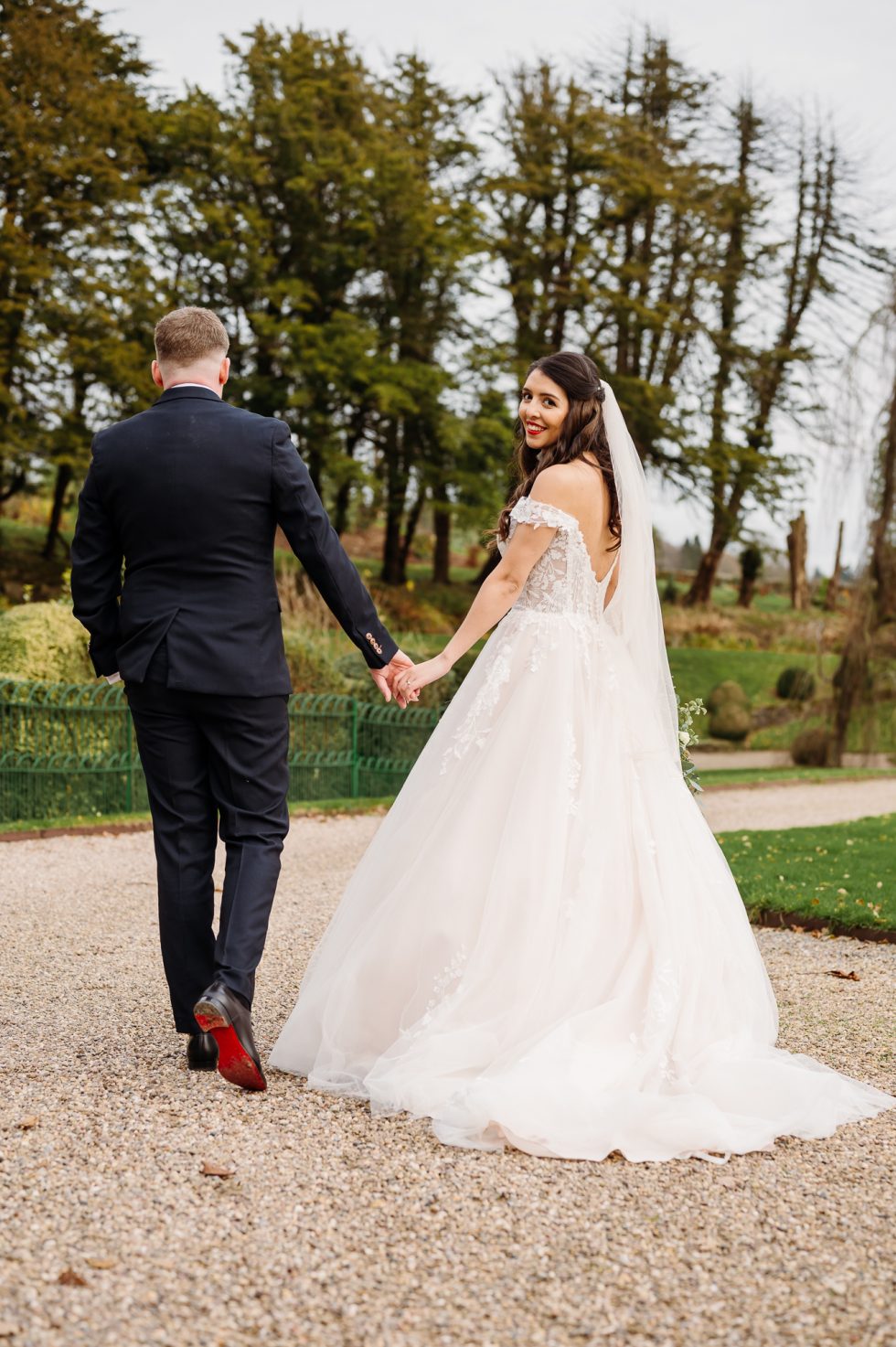 Bride and groom walking through the grounds at Browsholme Hall. The bride is looking back at the camera
