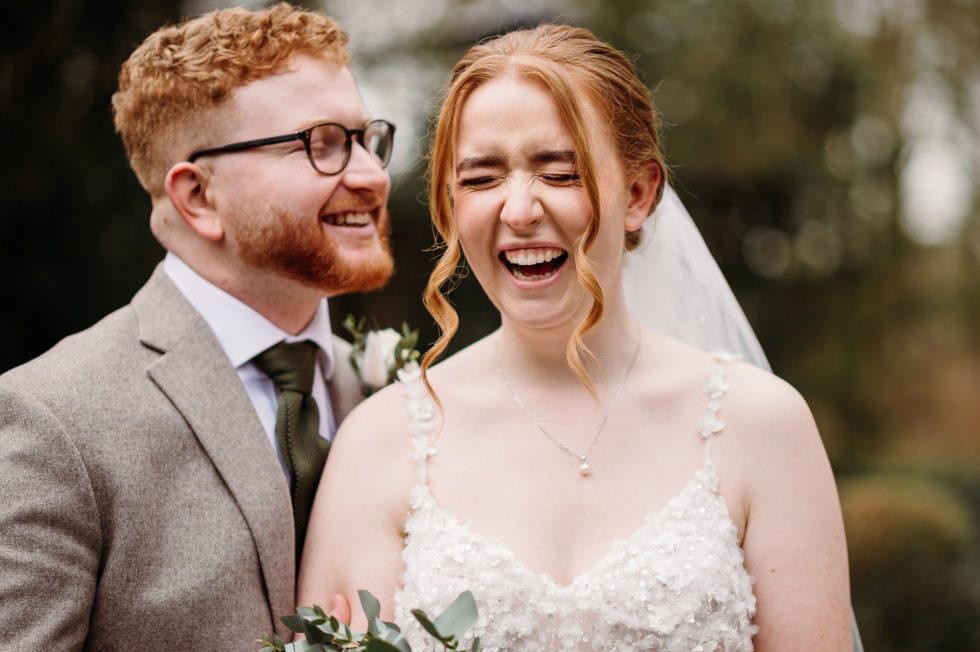 Bride laughing as her groom is telling her a secret and captured by Bartle Hall wedding photographer