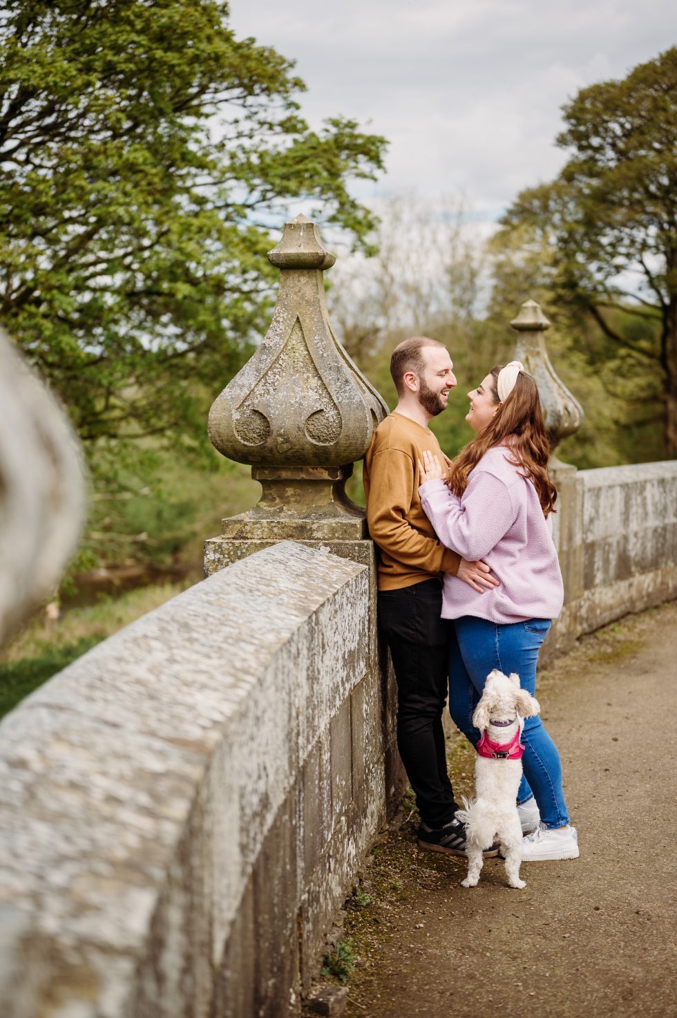Couple leaning on a wall and their dog is jumping up at them