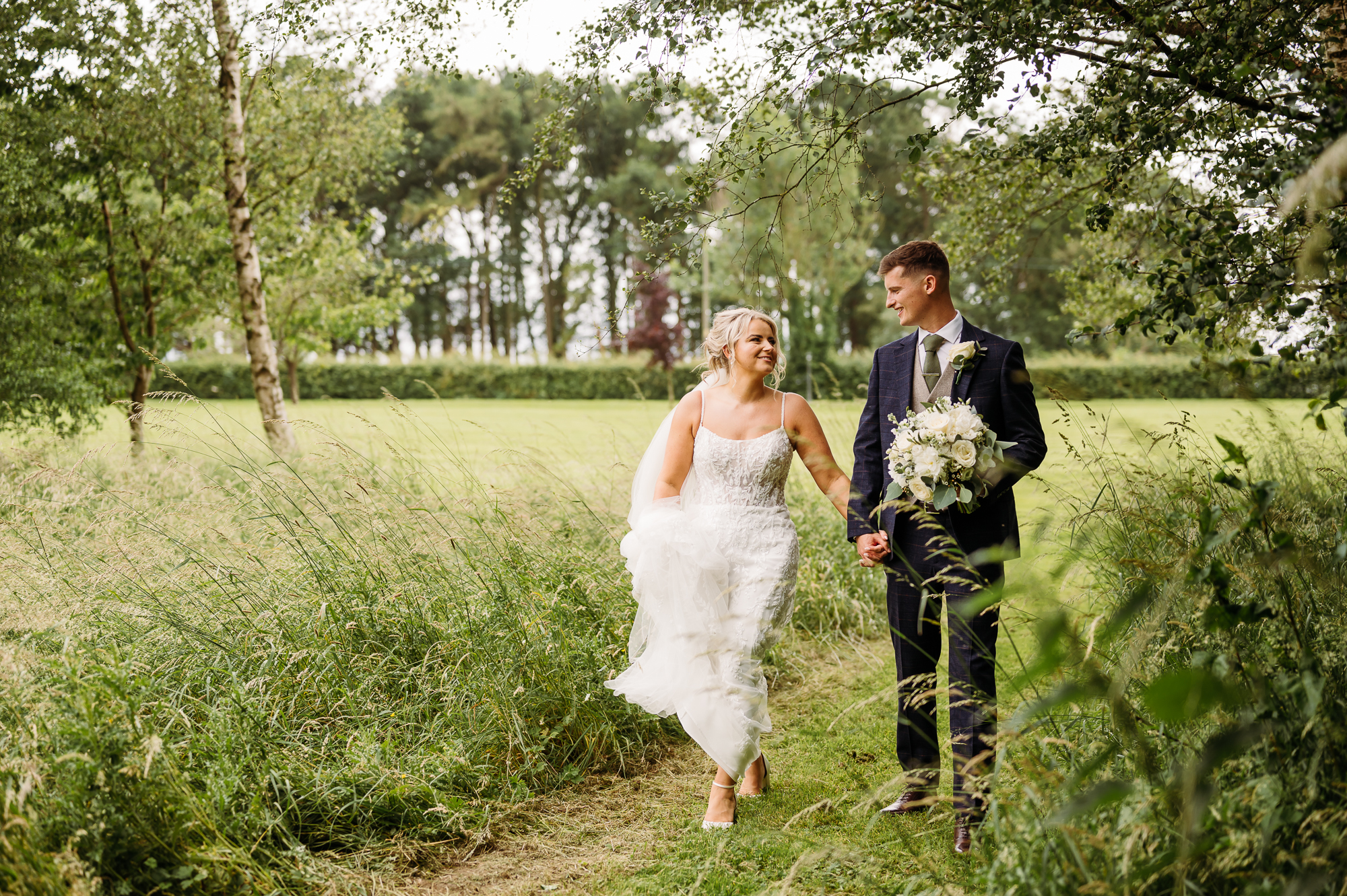 Bride and groom walking through the long grass at Stirk House