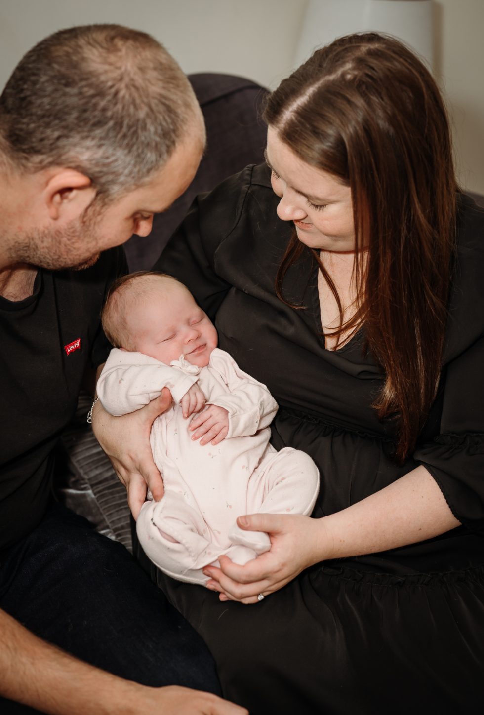 Mum and dad looking at their new daughter by Natural newborn photographer