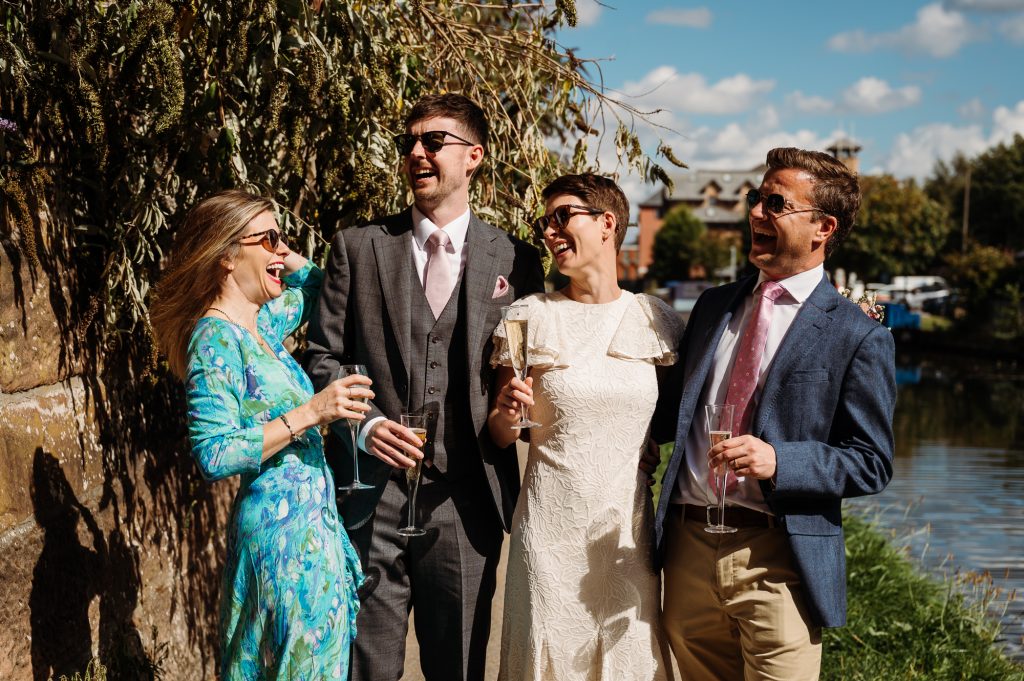 Bride and groom laughing with guests by a canal by relaxed Lancashire wedding photographer