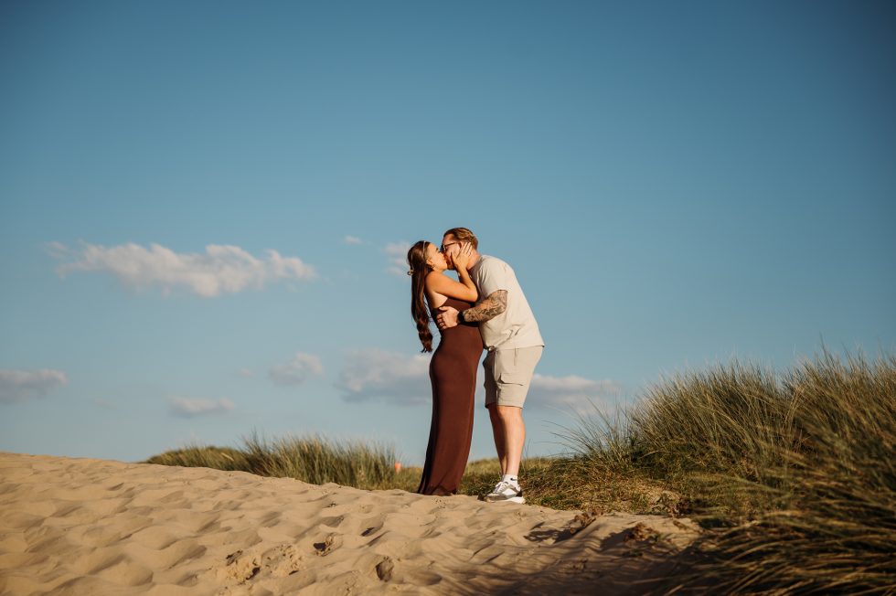 Lancashire Beach Proposal Shoot. Newly engaged couple kissing on sand dunes