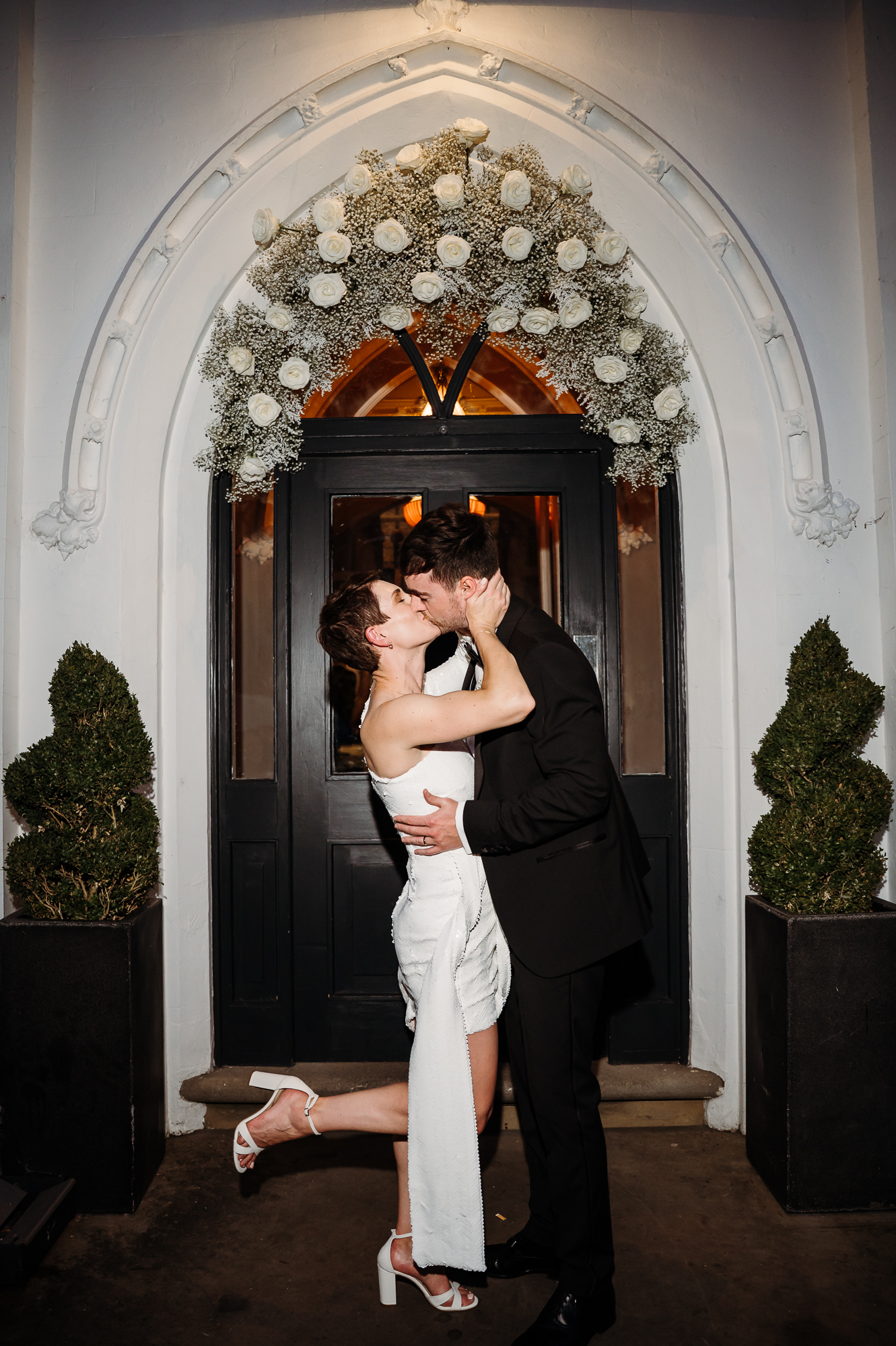 Bride and groom kissing in the doorway. Bride is kicking a foot up by Didsbury House wedding Photographer