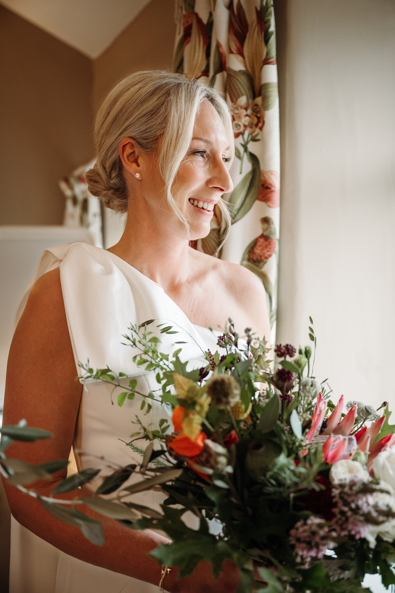Gorgeous blonde bride holding her wedding bouquet and looking out of the window