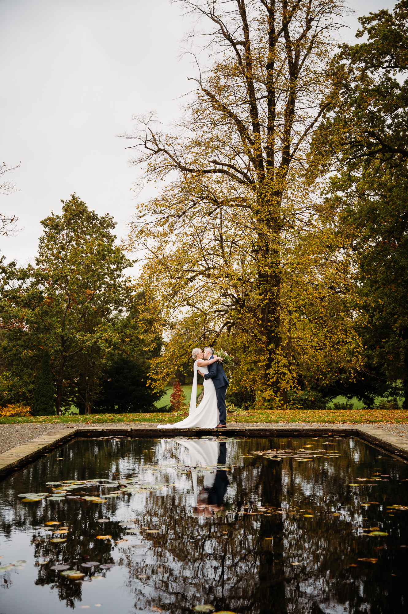Groom is drip kissing his new bride by the lily pond at Browsholme Hall.