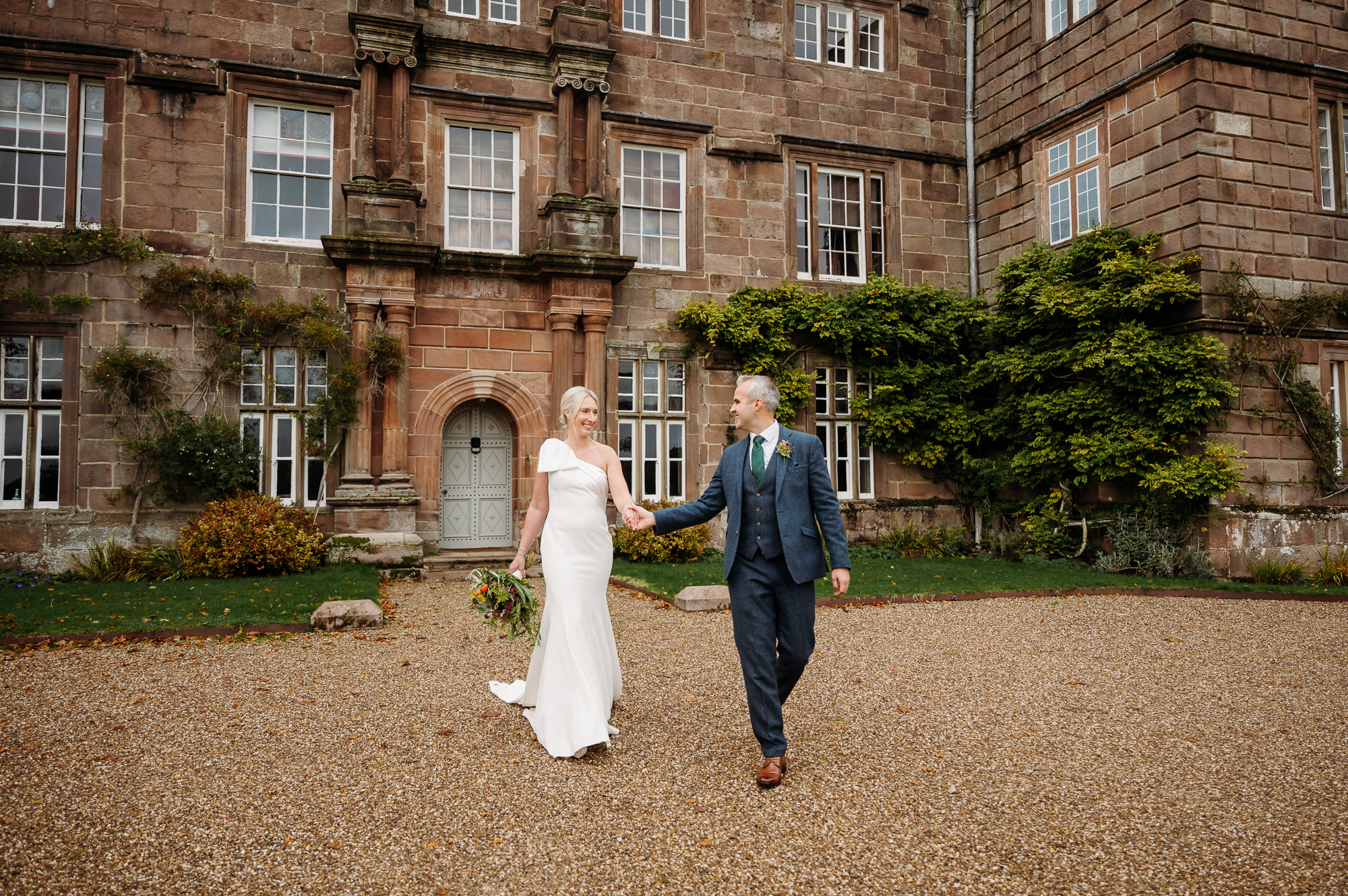 Groom is leading his bride along the gravel in from of Browsholme Hall.