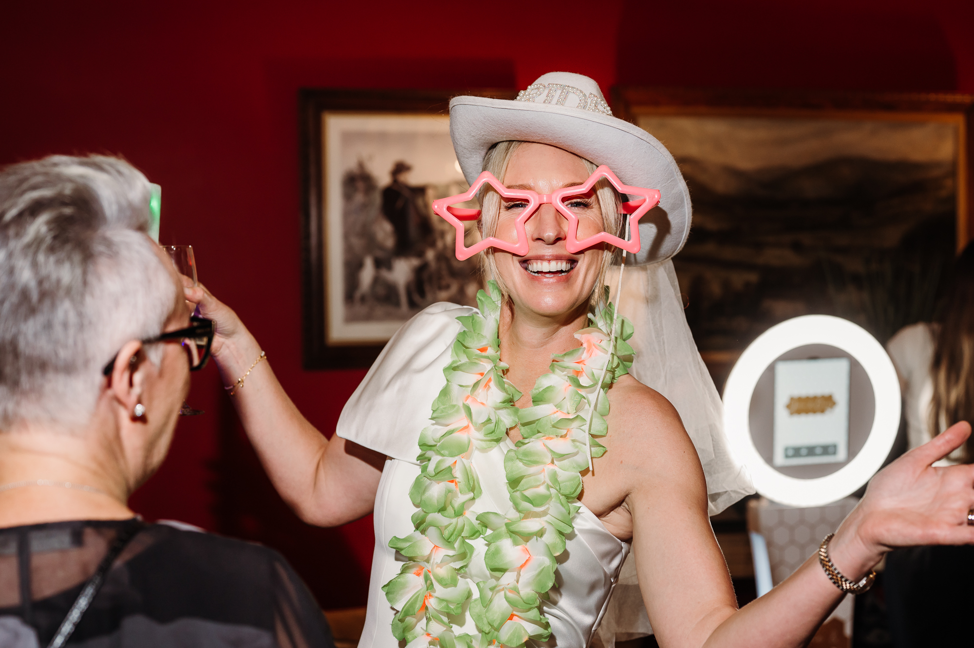 Bride is having fun with the Photo Booth. She has pink glasses and a cowboy hat on.