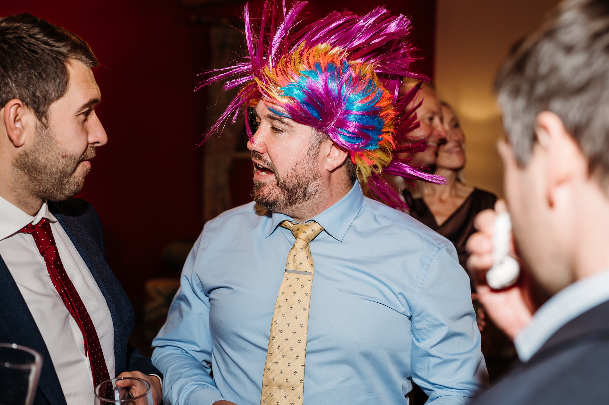 Wedding guests laughing and the man has a multi coloured wig on.