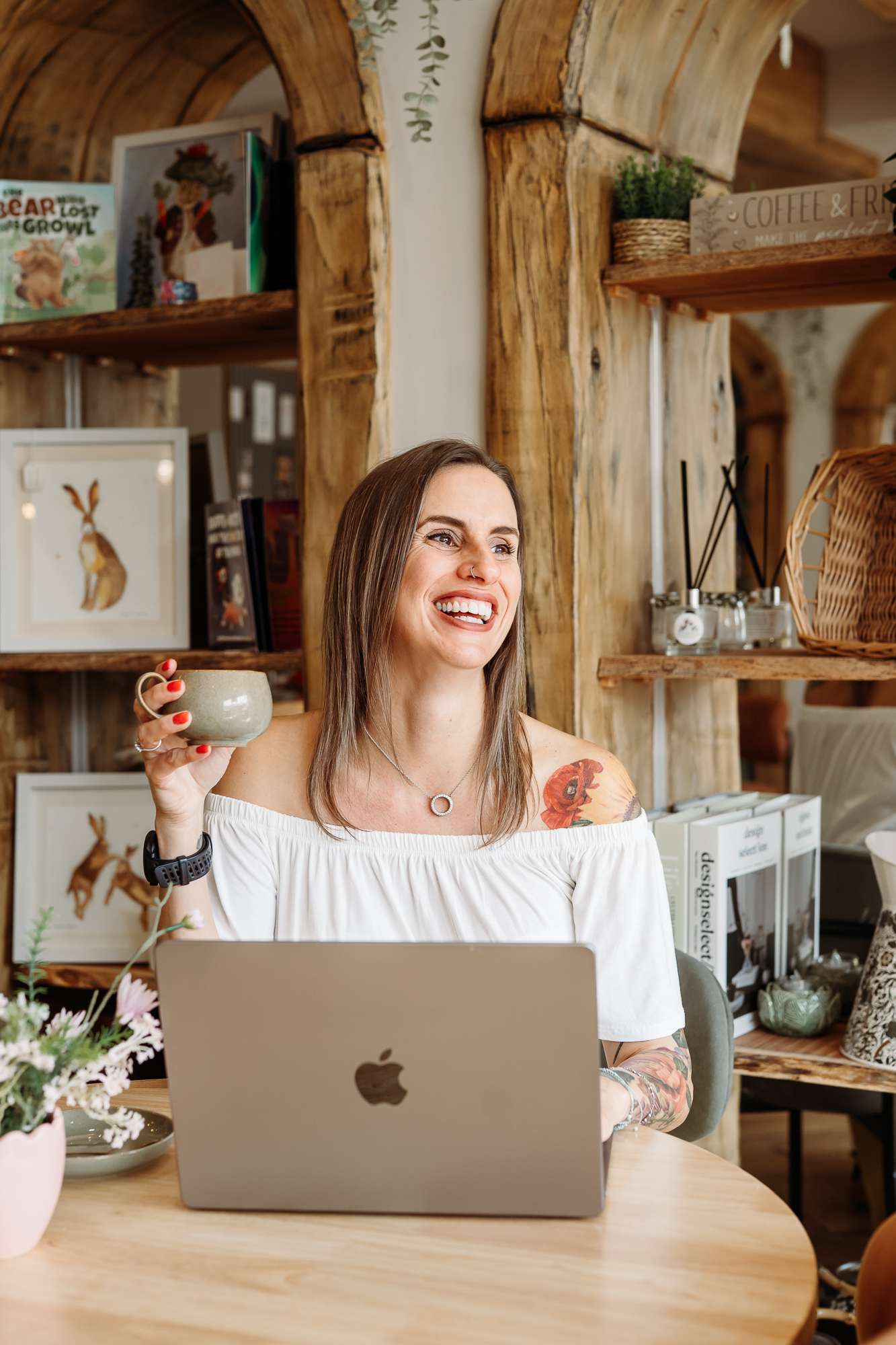 Lancashire wedding photographer, Jane Green is sat holding a cup of coffee behind her laptop and she is looking out of the window, laughing 