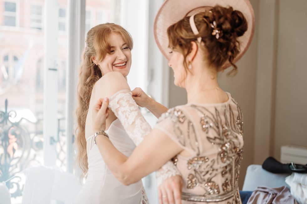 Gorgeous shot of brides mother helping the bride with lace sleeves on her dress