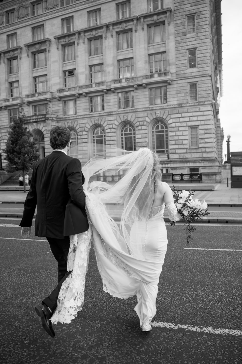 Black and white image of bride and groom walking across the road in Liverpool by by Lancashire wedding photographer